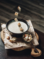 Cream of mushroom soup with white croutons. Soup in a dark plate. Croutons are fired from above. Hot food. Menu for cafes and restaurants. Light food. Dishes for lunch.