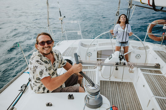 Man maneuvering with winch while woman driving sailboat in sea