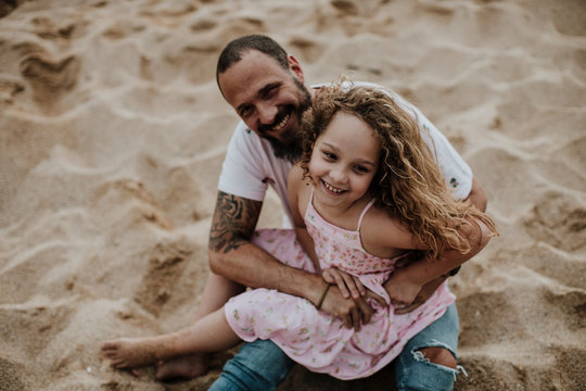 Daughter sitting on father's lap while playing at beach