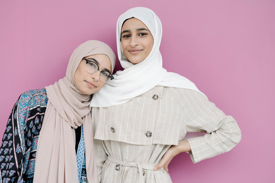 Muslim sisters standing together against purple background