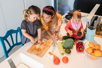 Baby girl sitting on island while mother looking at daughter chopping vegetables in kitchen
