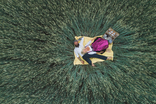 Aerial view of mature couple lying on blanket amidst green cornfield
