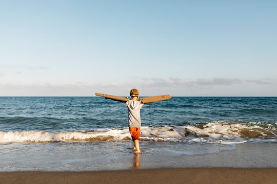 Boy wearing aircraft wings while standing with arms outstretched at beach