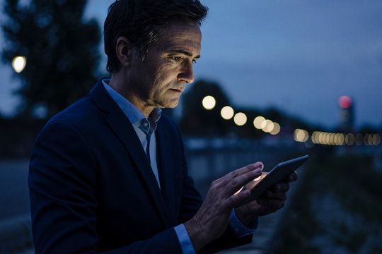 Mature businessman using tablet on a promenade at dusk