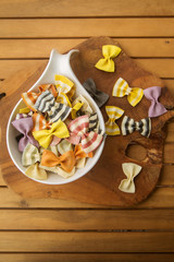 dry multicolored Italian handmade macaroni called farfalle, close-up in a white deep dish on a wooden background