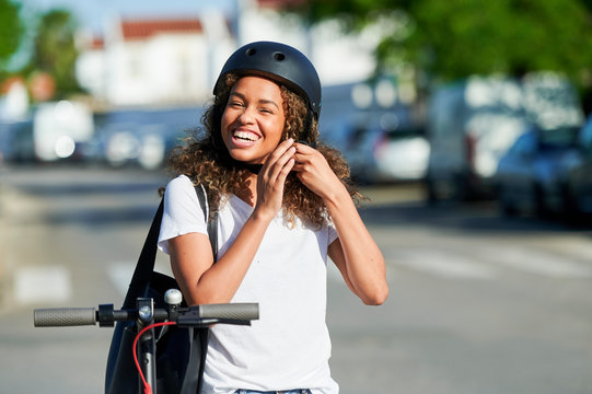 Cheerful woman wearing helmet while standing with electric push scooter during sunny day