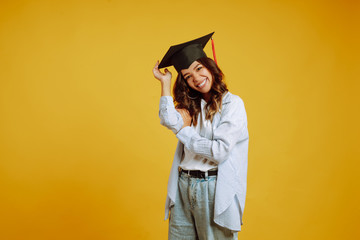 Graduate woman in a graduation hat on her head posing on a yellow background. Study, education, university, college, graduate concept.