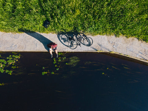 Aerial view of mid adult man with bicycle sitting at river coast during sunny day