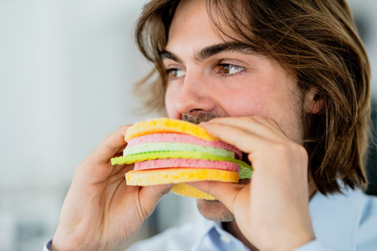 Close-up of businessman looking away while eating sponge cloth burger in cafe