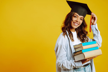 Portrait of young African American woman with books posing on a yellow background. Graduation,...