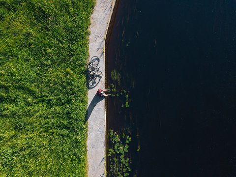 Drone shot of man with bicycle sitting at river coast during sunny day