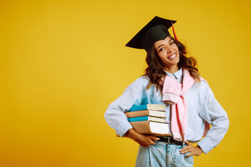 Portrait of young African American woman with books posing on a yellow background. Graduation, university, college, distance education concept.