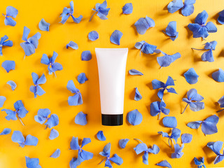 Top view of mockup light pink squeeze bottle plastic tube with black cap and petals of blue hydrangea flowers on a textured bright orange background. Bottle for branding and label. Natural organic spa