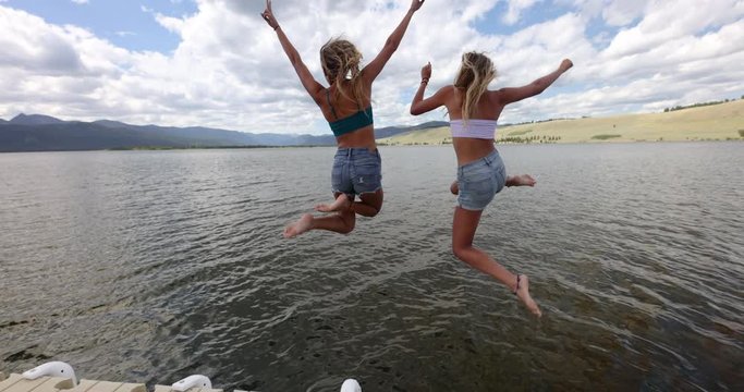 Young woman waving other to follow as they run and jump off dock into lake on summer vacation.