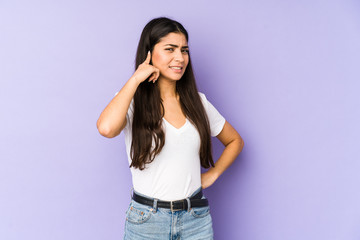 Young indian woman isolated on purple background covering ears with hands.