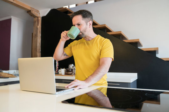 Man drinking coffee while using laptop on kitchen island at home