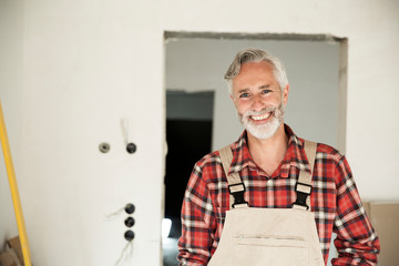 Smiling construction worker wearing overalls standing against wall in constructing house