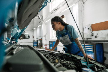 Get right help. Young african american woman, professional female mechanic looking, examining under hood of car at auto repair shop