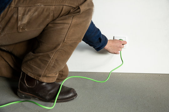 Close-up of technician inserting plug in outlet at constructing house