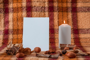 lit candle on old checkered blanket with orange red and brown patterns.dry leafs. autumn background. plain white sheet of paper.  dry fruits