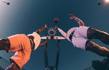 Male friends playing basketball against clear sky in court at night