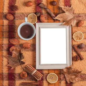 cup of coffee on old checkered blanket with orange red and brown patterns.dry leafs. autumn background. wood photo frame with plain white sheet.  dry fruits