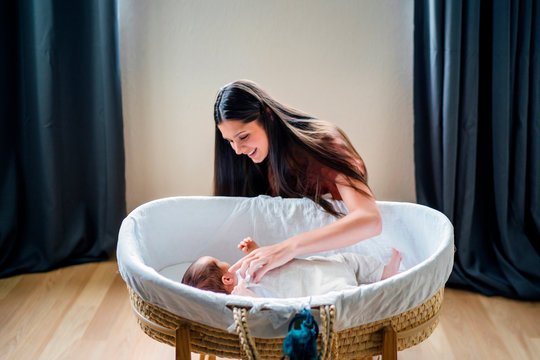 Happy mother looking at baby boy lying in crib at home