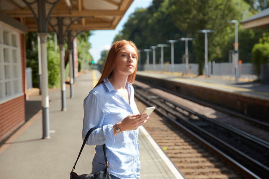 Young woman holding smart phone while standing at railroad station platform