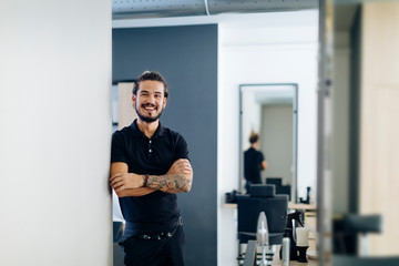 Confident male barber standing arms crossed in hair salon