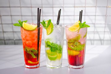Three refreshing summer cocktails in glasses with tubes on the bar rack.