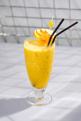 A glass of tasty fresh fruit yellow cocktail with a tube.