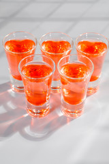 Red alcoholic shot drinks in glasses in a row on the bar count.