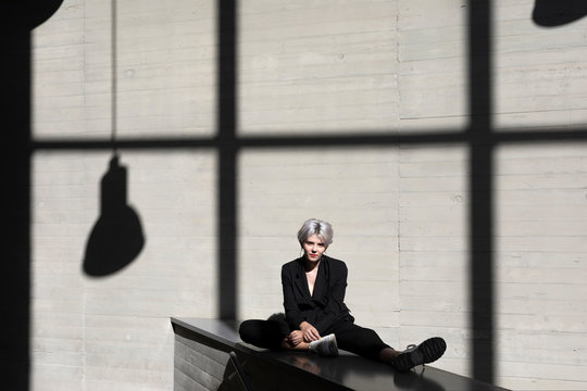 Female professional wearing black suit relaxing against sunlight and shadow in background at office