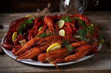
Boiled crayfish with dill and lemon on a white plate standing on a wooden table