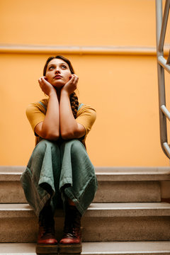 Young woman wearing jumpsuit leaning on orange wall and looking up