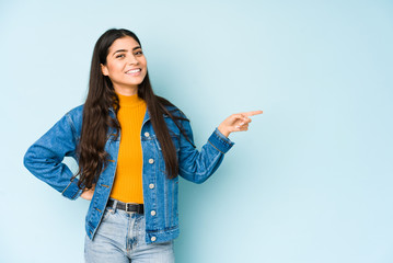 Young indian woman isolated on blue background smiling cheerfully pointing with forefinger away.