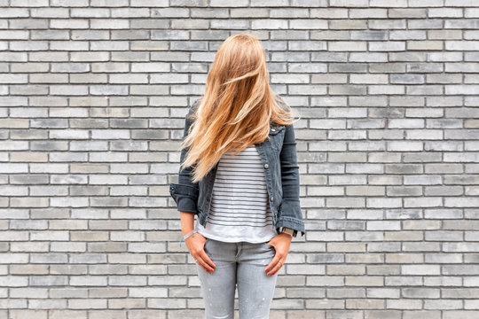 Fototapeta Woman with hair in front of face standing against gray brick wall