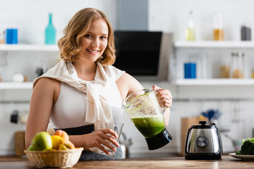 selective focus of young woman holding blender with mixed smoothie near glass