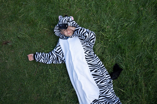 Boy wearing zebra costume lying on grassy land in yard