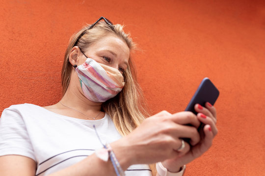 Woman wearing mask using smart phone while standing against orange wall