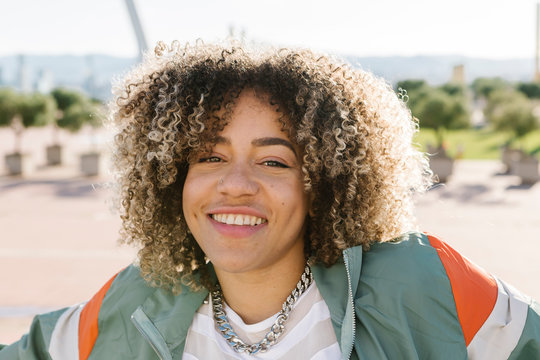 Happy young woman with curly highlighted hair during sunny day