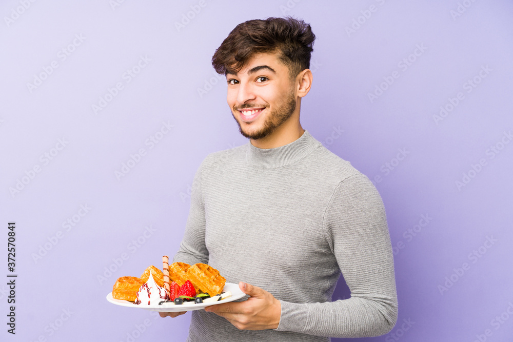 Wall mural young arabian man holding a waffle isolated laughing and having fun.