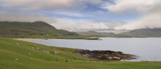 The lost Vally and Silver Strand beach of Uggool, county Mayo, Ireland. Nobody, Panorama image, green field, and beach, mountains in the background covered with low clouds.