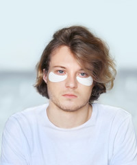 Anti-aging eye therapy. young man taking care of his undereye wrinkles applying facial mask. Dark Circles.Eye patches.	