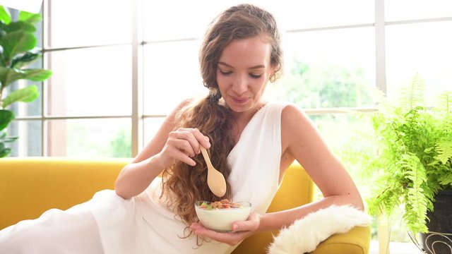 Healthy young woman lying on a couch and eating yogurt looking relaxed and comfortable.