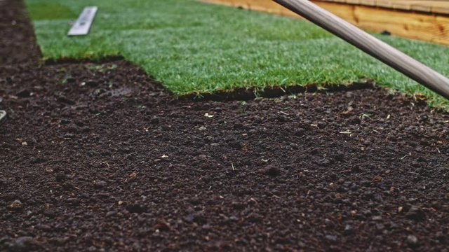 Gardener Grading Out Soil With A Rake. SLOW MOTION. Unrecognizable persons' hands leveling out the ground, laying perfect sod, planting green grass lawn. Man working on a landscape design. 