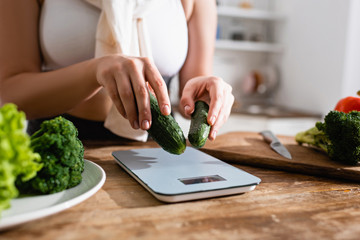 cropped view of woman putting cucumbers on kitchen scales
