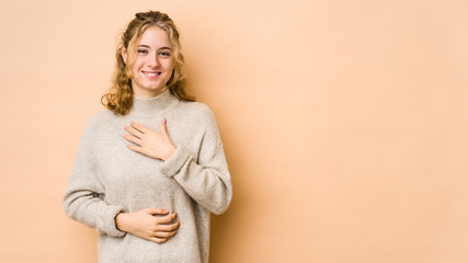 Young caucasian woman isolated on beige background laughs happily and has fun keeping hands on...