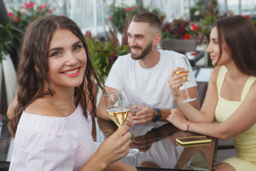 Charming happy woman smiling with a glass of wine in her hand, enjoying celebrating with her friends at the bar