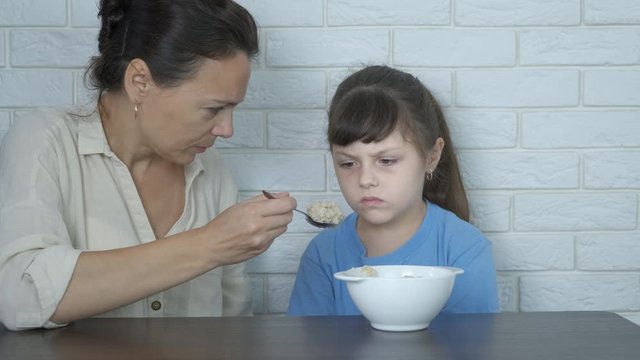 Feed with porridge. Mother feeds her daughter oatmeal. The little girl refuses to eat porridge.